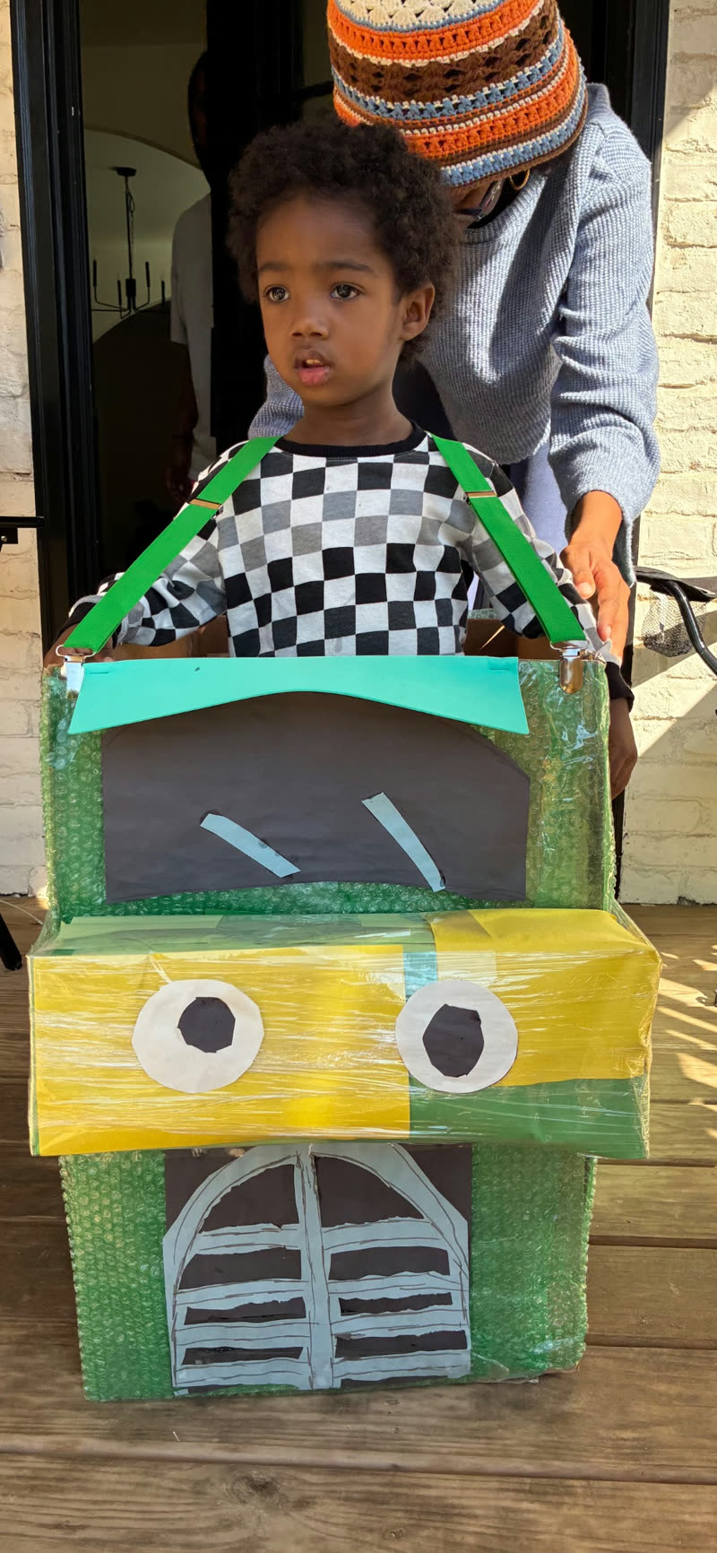 A young participant wears a handmade cardboard truck costume with green suspenders