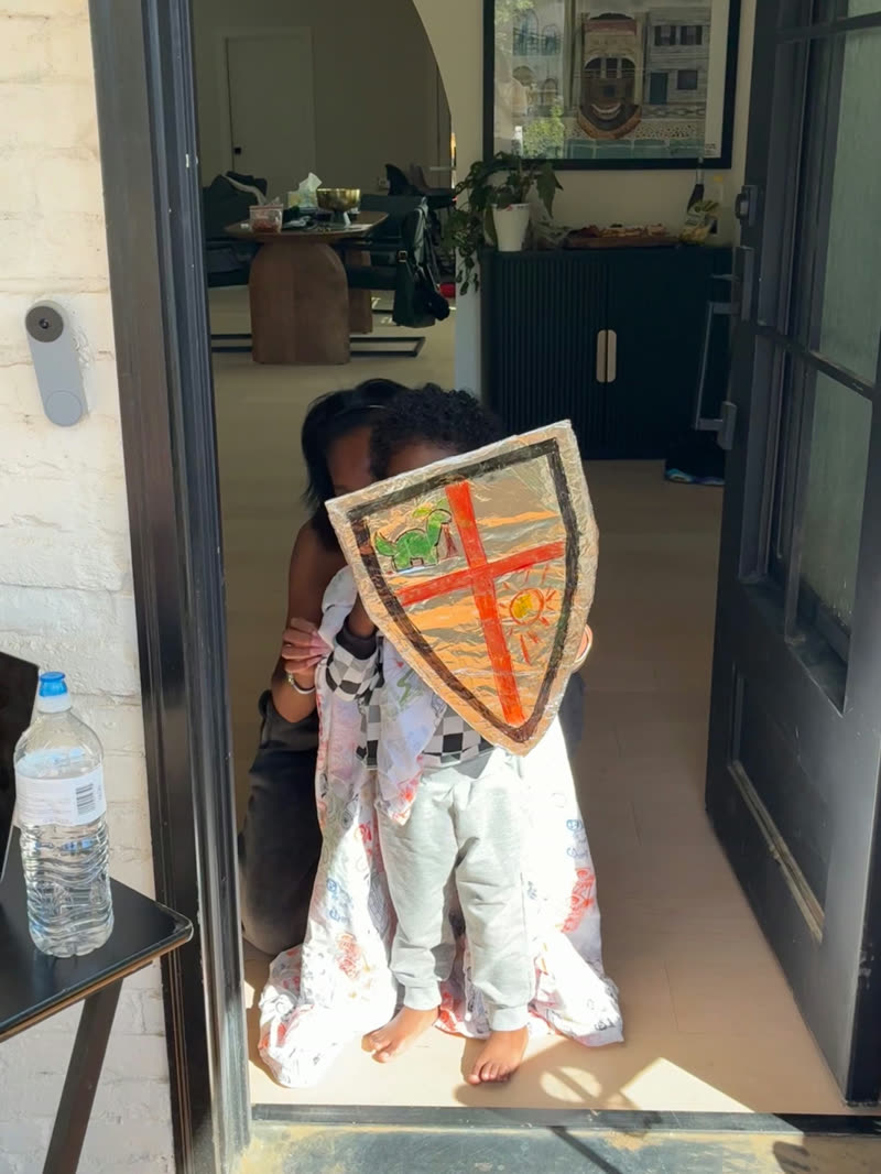 A young participant holds a handmade foil shield decorated with a dinosaur and sun