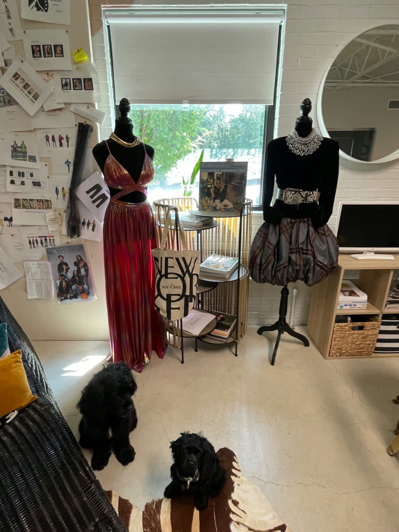 A design studio with dressed mannequins, a moodboard wall, and two dogs resting on the floor