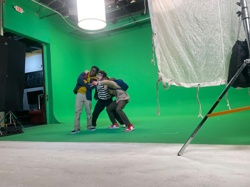 Three young participants pose together on a green-screen film set