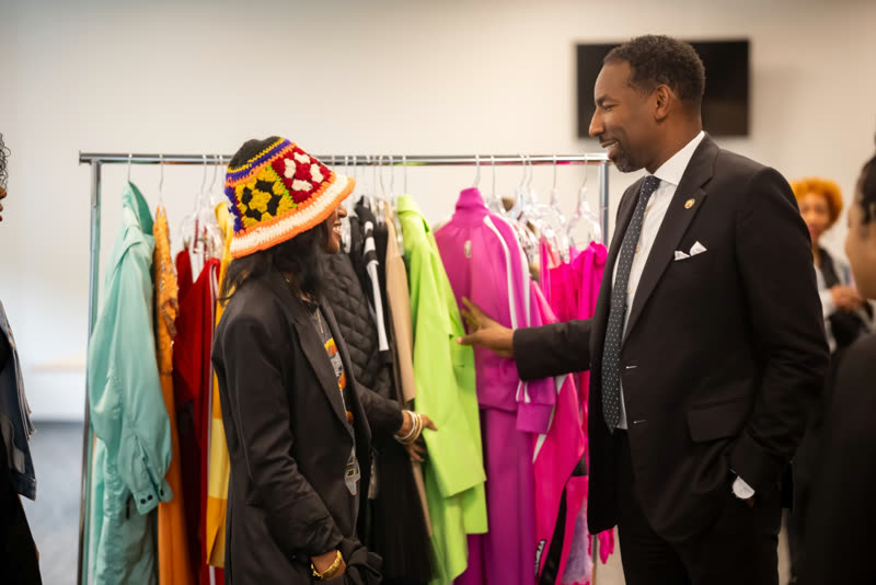 An industry professional and a young creative talk through garments on a colorful rack