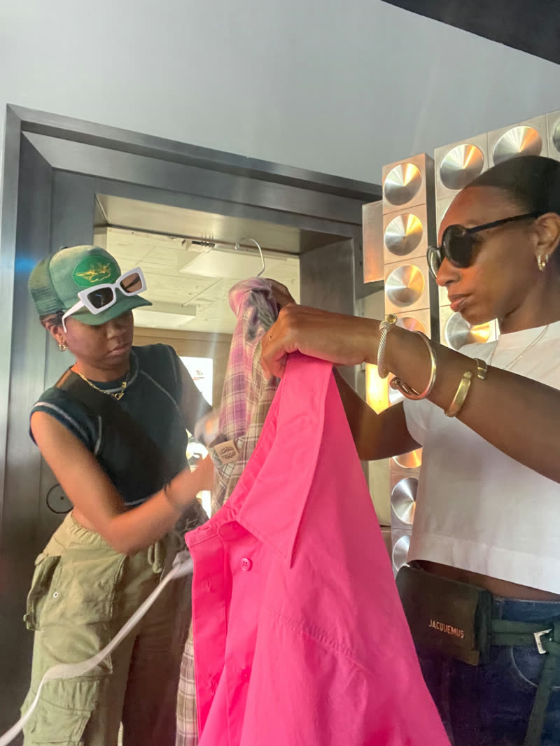 Two people steam and prepare a bright pink garment in a dressing area